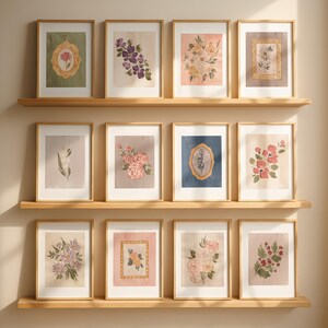 May include: A collection of framed floral art prints displayed on wooden shelves. The prints feature watercolor illustrations of various flowers in soft pastel colors, including roses, lilacs, and other botanical designs. The frames are a light wood color.