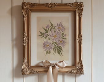 May include: A framed floral print featuring a bouquet of lavender flowers with green leaves. The print is in a gold ornate frame with a beige satin bow tied at the bottom. The artwork is displayed against a white paneled wall.