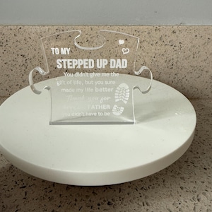 May include: Clear acrylic puzzle piece with the text "TO MY STEPPED UP DAD". The puzzle piece has a heart and a footprint design. The text reads "You didn't give me the gift of life, but you sure made my life better. Thank you for being a FATHER you didn't have to be."