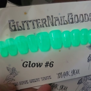 May include: A set of ten green glow-in-the-dark false nails. The nails are arranged in a row on a white card with the text "GlitterNailGoods" and "Glow #6" printed on it.