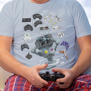 May include: A father and son are sitting on a sofa, both holding video game controllers. The father is wearing a light blue t-shirt with a graphic of a robot holding various video game controllers. The son is wearing a white and blue pyjama top with a rocket ship pattern.
