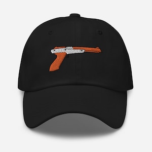 May include: A black baseball cap with an embroidered orange and white video game gun on the front.