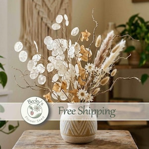 May include: A bouquet of dried botanicals including translucent silver dollar plant stems, tan pampas grass, and small white flowers arranged in a round, cream-colored ceramic vase with a textured geometric chevron pattern in light brown.
