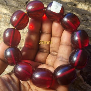 May include: A red, round bead bracelet with 21mm beads. The bracelet is made of glass and has a shiny finish.
