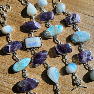 May include: Three silver bracelets with various gemstone charms. The charms include amethyst, moonstone, and blue lace agate. The bracelets have a toggle clasp.
