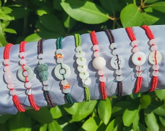 May include: Eight jade bracelets with red string and various jade charms, including a round charm, a round charm with a hole in the center, a round charm with a design, a round charm with a design, a round charm with a design, a round charm with a design, a round charm with a design, and a round charm with a design.