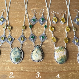 May include: Five sets of gemstone jewelry, each including a necklace and earrings. The necklaces feature large, oval or teardrop-shaped stones in shades of green, yellow, and brown, set in silver-toned metal. The earrings have matching stones.