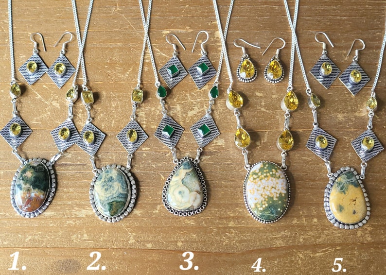 May include: Five sets of gemstone jewelry, each including a necklace and earrings. The necklaces feature large, oval or teardrop-shaped stones in shades of green, yellow, and brown, set in silver-toned metal. The earrings have matching stones.