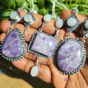 Puede incluir: Tres collares de plata con colgantes de piedras preciosas p&uacute;rpuras y blancas. Los colgantes tienen forma de l&aacute;grima, cuadrado y &oacute;valo. Los collares est&aacute;n en una mano, y los n&uacute;meros 6, 7 y 8 est&aacute;n escritos en la mano.