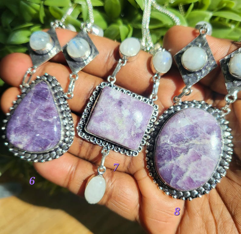 Puede incluir: Tres collares de plata con colgantes de piedras preciosas p&uacute;rpuras y blancas. Los colgantes tienen forma de l&aacute;grima, cuadrado y &oacute;valo. Los collares est&aacute;n en una mano, y los n&uacute;meros 6, 7 y 8 est&aacute;n escritos en la mano.