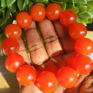 May include: A bracelet made of bright orange round beads. The beads are smooth and glossy.
