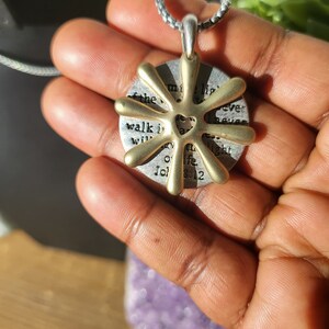 May include: A gold-toned pendant necklace with a circular charm featuring a heart design and the text "Walk in the light of the Lord, I never walk alone, John 8:12".