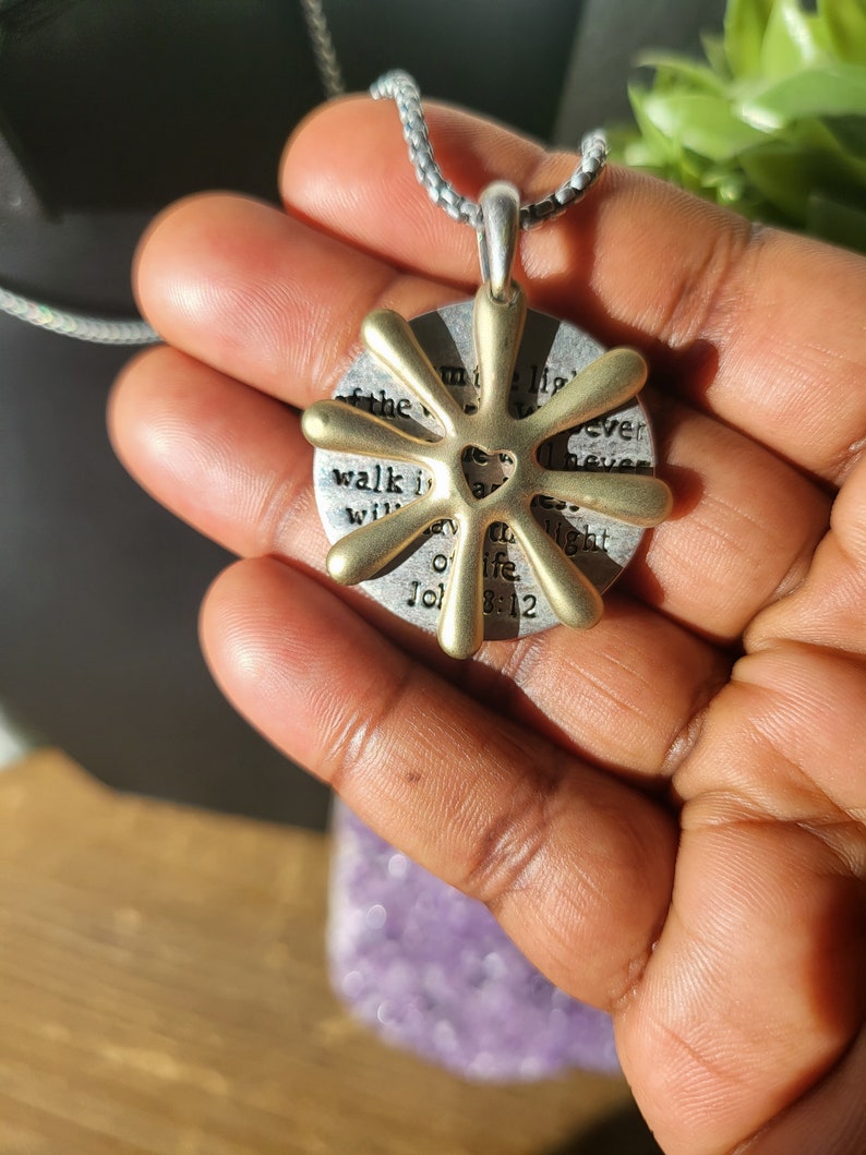 May include: A gold-toned pendant necklace with a circular charm featuring a heart design and the text "Walk in the light of the Lord, I never walk alone, John 8:12".