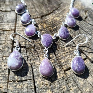 Puede incluir: Un conjunto de collar y pendientes de plata con gotas de piedras preciosas p&uacute;rpuras. El collar tiene un colgante con tres gotas y los pendientes tienen una gota cada uno.