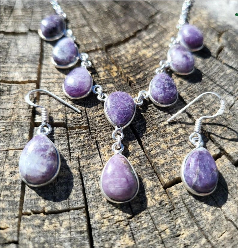 Puede incluir: Un conjunto de collar y pendientes de plata con gotas de piedras preciosas p&uacute;rpuras. El collar tiene un colgante con tres gotas y los pendientes tienen una gota cada uno.