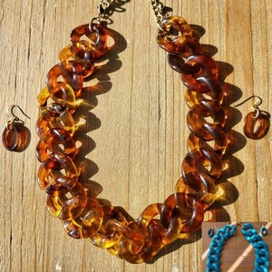 May include: A chunky, amber-colored plastic chain necklace with matching earrings. The necklace is made of large, interlocking links. The earrings are simple and dangle.