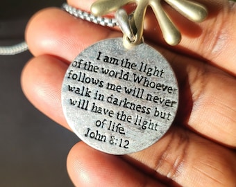 May include: Silver pendant necklace with a round charm that reads "I am the light of the world. Whoever follows me will never walk in darkness but will have the light of life. John 8:12".
