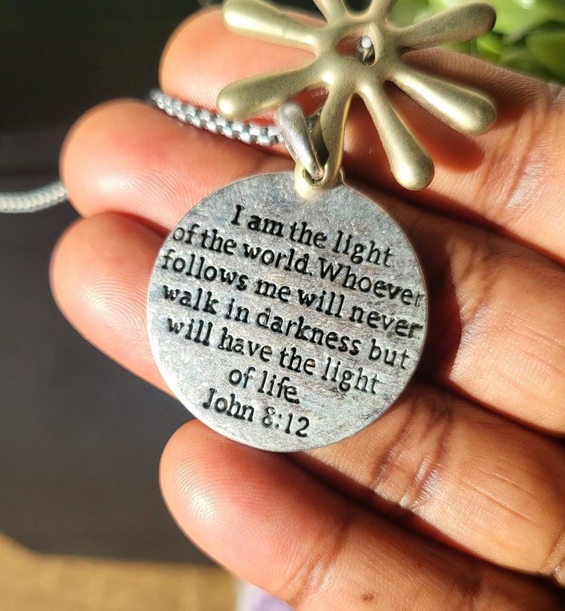 May include: Silver pendant necklace with a round charm that reads "I am the light of the world. Whoever follows me will never walk in darkness but will have the light of life. John 8:12".