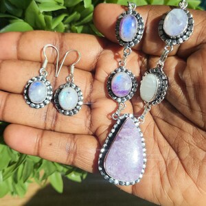 Puede incluir: Un conjunto de collar y pendientes de plata con piedras preciosas de piedra lunar y amatista. El collar presenta un colgante de amatista en forma de l&aacute;grima y tres piedras de luna redondas. Los pendientes son aros de plata con piedras de luna redondas.