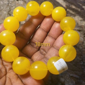 May include: A yellow beaded bracelet with 18mm beads. The bracelet is made of round, smooth beads.