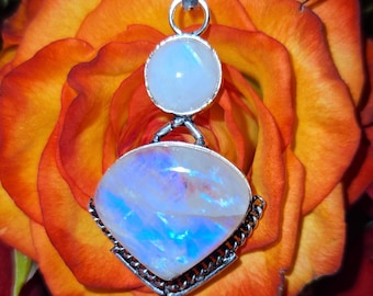 May include: A silver pendant necklace featuring a large, iridescent, teardrop-shaped moonstone and a smaller, round moonstone. The pendant hangs against a backdrop of a vibrant orange and yellow rose.