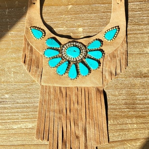 May include: A brown suede necklace with turquoise stones and fringe. The necklace is in the shape of a crescent moon.