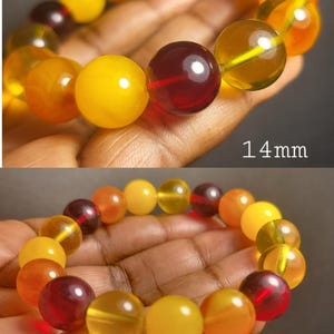 May include: A bracelet made of amber beads in shades of yellow, orange, and red. The beads are round and have a smooth, polished finish. The bracelet is 14 mm wide and 12 mm wide.