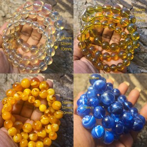 May include: Four strands of beads in different colors and sizes. The beads are round and have a smooth, polished finish. The beads are arranged in a circle and are held in a hand. The beads are 10mm, 12mm, 14mm, and 16mm in diameter.