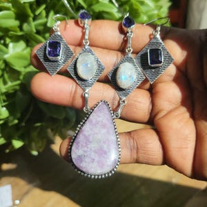 Puede incluir: Un collar de plata con un colgante de piedra preciosa lavande en forma de l&aacute;grima y pendientes a juego con piedras preciosas de piedra lunar y amatista.