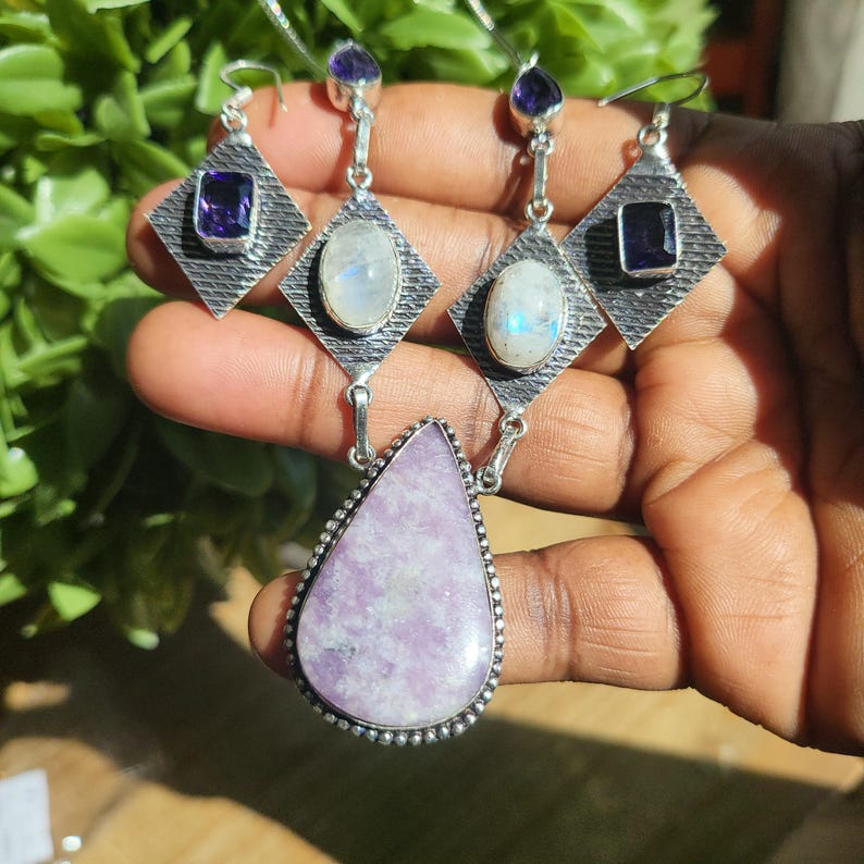 Puede incluir: Un collar de plata con un colgante de piedra preciosa lavande en forma de l&aacute;grima y pendientes a juego con piedras preciosas de piedra lunar y amatista.