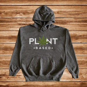 May include: A dark gray hooded sweatshirt with a white graphic that says "PLANT BASED" with a green marijuana leaf in the middle of the word "PLANT".