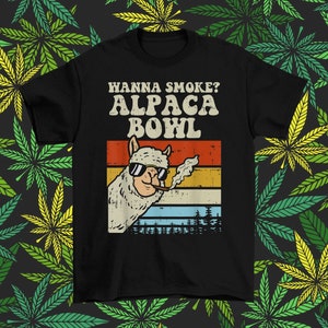 May include: Black t-shirt with a retro-style graphic of an alpaca smoking a joint. The text "Wanna Smoke? Alpaca Bowl" is printed in white on the shirt.