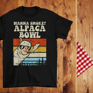 May include: Black t-shirt with a vintage-style graphic of an alpaca wearing sunglasses and smoking a cigar. The text "Hanna Smoke? Alpaca Bowl" is printed in white above the alpaca.