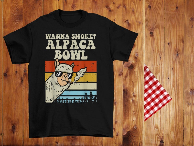 May include: Black t-shirt with a vintage-style graphic of an alpaca wearing sunglasses and smoking a cigar. The text "Hanna Smoke? Alpaca Bowl" is printed in white above the alpaca.