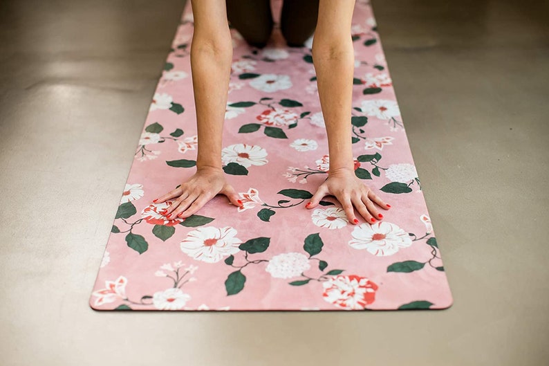 May include: A pink yoga mat with a floral pattern featuring white and red flowers and green leaves. The mat is on a light gray surface.