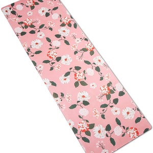May include: A pink yoga mat with a floral pattern featuring white and red flowers. The mat has a textured surface.