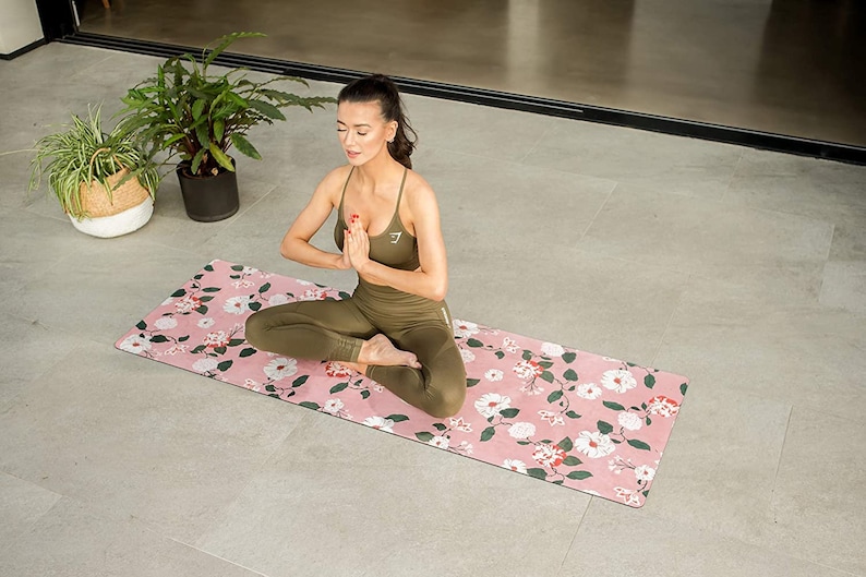 May include: A woman sits in a yoga pose on a pink floral yoga mat. She is wearing a green sports bra and leggings.