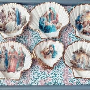 Può includere: Sei conchiglie bianche con bordi dorati, ciascuna decorata con una diversa scena della Natività di Natale. Le scene includono i tre re magi, la sacra famiglia e i pastori.