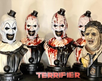 May include: A collection of horror-themed busts, including a clown with white makeup and a top hat, and a figure with a chainsaw. The word "TERRIFIER" is displayed in red letters at the bottom.