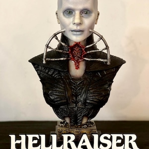 May include: A detailed bust of a character from the movie "Hellraiser." The figure has pale skin, a bald head, and a distinctive facial expression. The bust features a black outfit and a decorative metal collar. The word "HELLRAISER" is displayed in white block letters.
