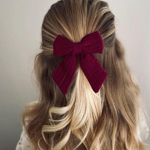 Può includere: Un fermaglio per capelli con fiocco color borgogna per ragazze con capelli lunghi, ondulati e biondi.