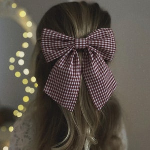 May include: A red and white gingham bow tied in a large, voluminous knot. The bow is worn in a person's hair.