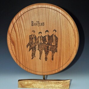 Könnte beinhalten: Eine runde Holzplakette mit einem schwarz-weißen Bild der Beatles, das darauf graviert ist. Die Plakette ist auf einem Holzständer montiert.