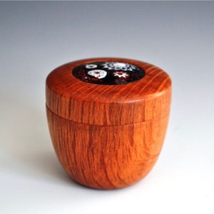 Könnte beinhalten: Eine Holzkiste mit einem runden Deckel. Der Deckel ist mit einem bunten Mosaik aus Glasstücken verziert. Die Kiste ist aus hellem braunem Holz mit einer Maserung.