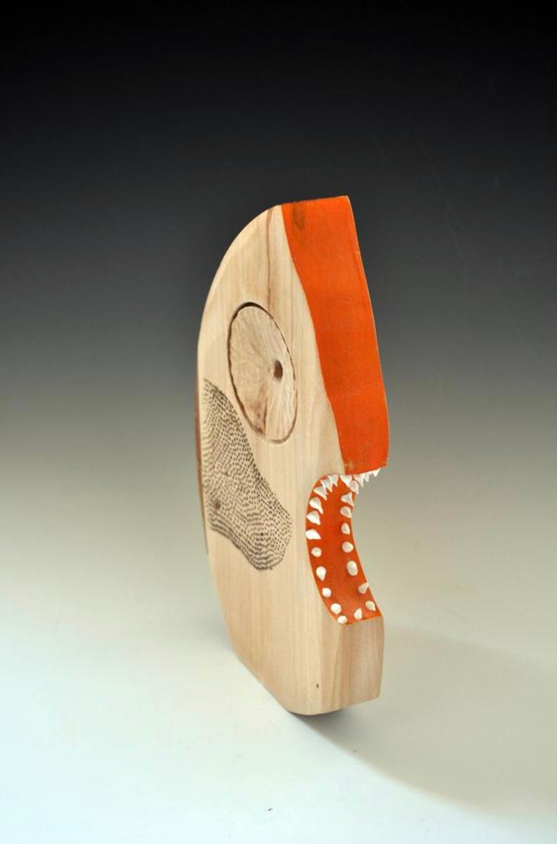 Puede incluir: Una escultura de madera de un pez con la boca abierta, pintada de naranja y blanco. El pez tiene un ojo grande y una fila de dientes.