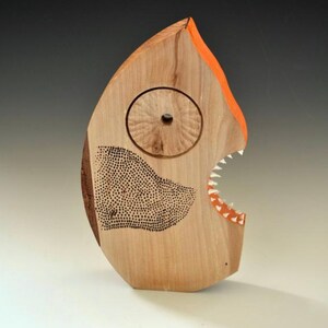 Puede incluir: Una escultura de madera de un pez con la boca abierta, pintada de naranja y blanco. El pez tiene un ojo circular y un patr&oacute;n de puntos negros y blancos en su cuerpo.