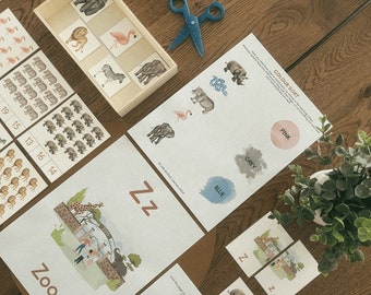 Op de afbeelding: Een set educatieve werkbladen en kaarten met dierenillustraties, waaronder een pagina voor het sorteren van kleuren met de tekst COLOUR SORT, een pagina met een dierentuinthema met de letter Z en een houten dienblad met kleine dierenkaarten.