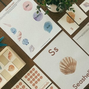 May include: A printable seashell themed educational activity set for kids. The set includes a color sort activity, a playdough mat, and a letter S flashcard with a seashell illustration. The text on the flashcard reads "Seashell".