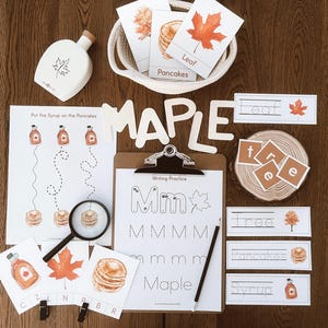 Peut inclure: Un ensemble éducatif sur le thème de l'automne, comprenant des cartes, des lettres en bois épelant "MAPLE" et des feuilles d'exercices d'écriture. Les illustrations représentent des feuilles d'érable, des crêpes et des bouteilles de sirop. Une bouteille en bois avec un motif de feuille est également incluse.