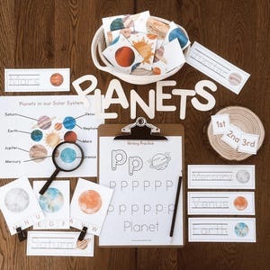 Puede incluir: Conjunto educativo con temática planetaria. Incluye tarjetas didácticas, un diagrama del sistema solar, letras de madera que deletrean "PLANETS" y una tabla con ejercicios de escritura. El conjunto presenta ilustraciones coloridas de planetas y una lupa.